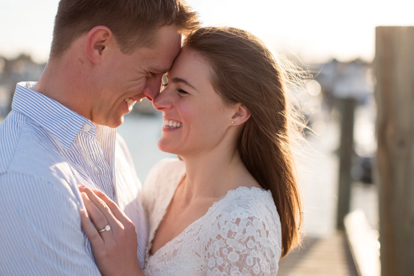 Newly engaged couple laughing forehead to forehead on a sunlit harbor dock